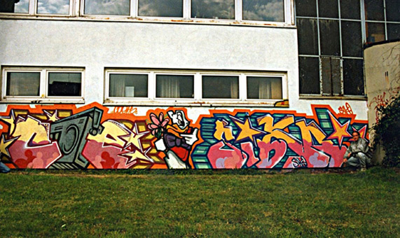 Auftrag Pfensig Wendorf, 1990. Ein Graffitiauftrag für die Gabelstaplerfirma Pfensig und Wendorf in Hamburg im Mürz 1990. Auftragsmalerei von der Mad Artists Cooperation, Sage und Siko Ortner sowie eine freie Wandgestaltung von Coe/Skero und Siko Ortner (direkt an der S-Bahn nähe Langenfelder Bahnhof, quasi als Dankeschön der Auftraggeber). Piece/Mural von Coe/Skero und Siko Ortner, charakter von Coe/Skero.