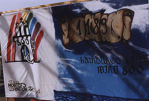 Projekt 800ter Hafengeburtstag Hamburg, Juni 1989. Ein Graffiti Projekt für Reisegewerbebetrieb Wilms, präsentiert beim 800sten Hafengeburtstag Hamburg 1989 und beim Hamburgurger Dom Frühjahr 1990. Projektausfhrung: Mad Artists Cooperation, Siko Ortner und seinen Graffitischülern Wizz und Adonis. Stancelgemälde der bedeutenden Gebäude Hamburgs auf einem Schiff. Stancelart, Sprühlack auf Folie ca. 3,90m X 18m, unter Nutzung von vielen 1-Fach-und Mehrfachstanceln. Teilansicht Symbol und Schrifrolle.