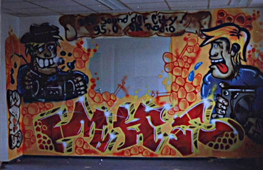 Graffitiliveakt zum 1 jährigen Geburtstag von OK Radio im Studio in Hamburg, Herbst 1989. Projektorganisation durch Herrn Claussen von OK Radio. Projektausführung von der mad artists cooperation, Wizz und Siko Ortner. Mural an der Studioaussenwand, das piece (2 charakter und ein MAC-style mit Schriftrolle) wurde während der Feierlichkeiten zum 1 jährigen Bestehen des Radiosenders fertiggestellt.  Fertiggestelltes piece.